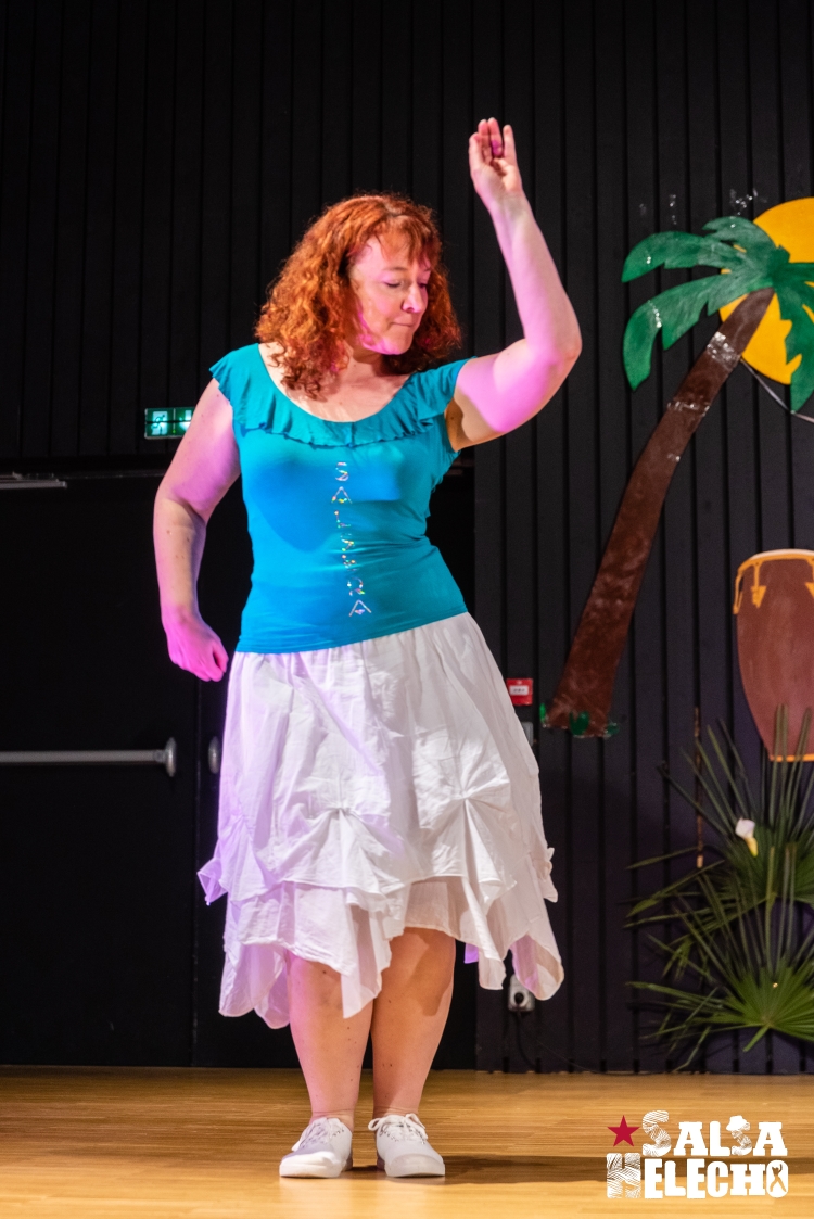 Femme vêtue d'une chemise bleue et d'une jupe blanche en train de danser.