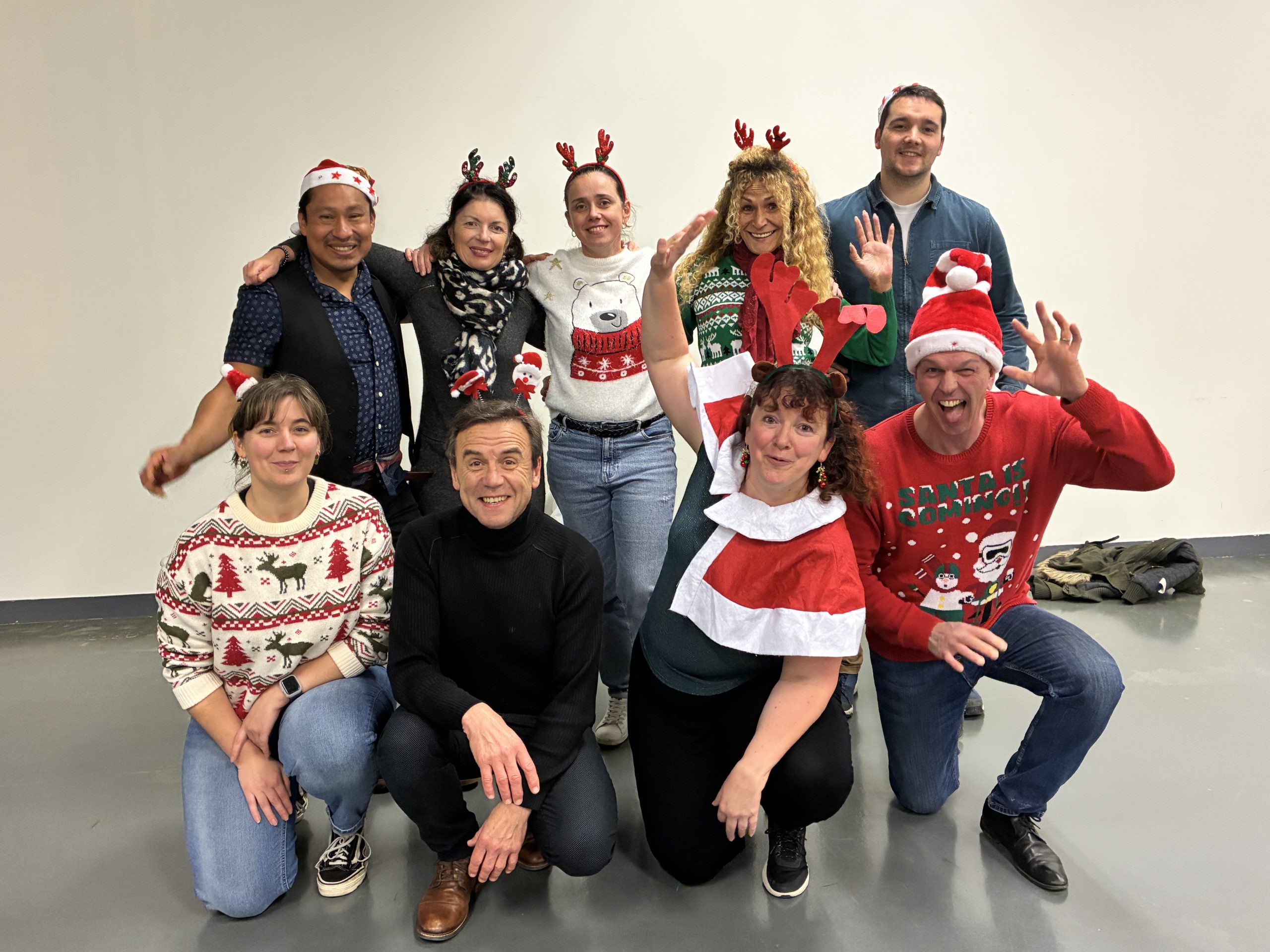 Un groupe de personnes en tenue et accessoires de Noël pose en souriant dans une salle, dans une ambiance festive et conviviale.