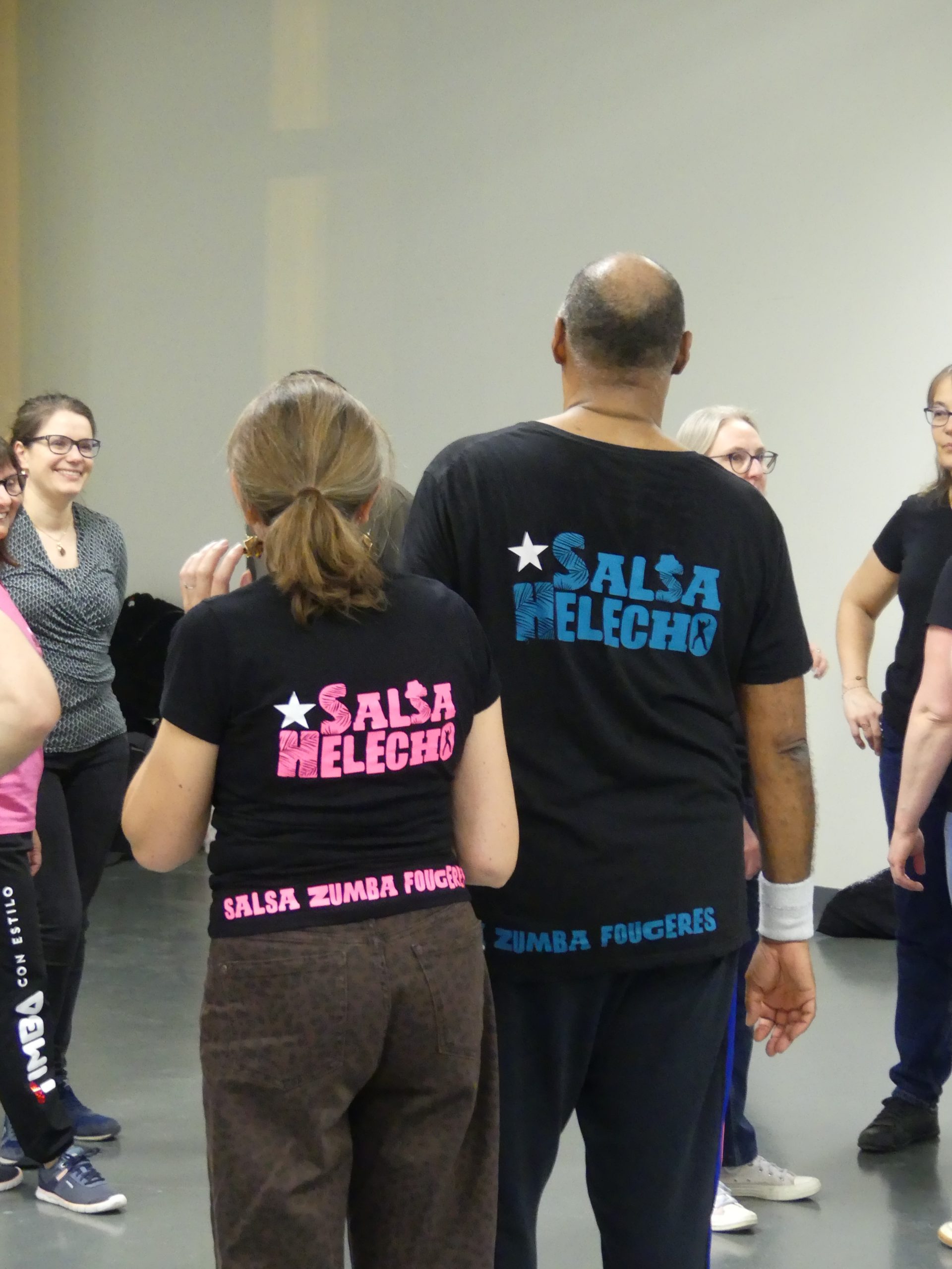 Plusieurs personnes dans une salle de danse, apprenant des mouvements sous l'œil attentif d'un professeur.