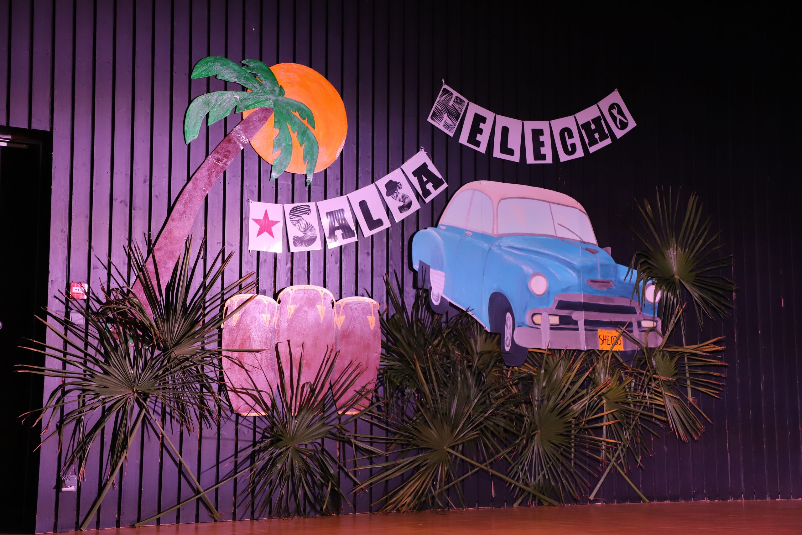 Une scène de spectacle avec une voiture et des palmiers, suggérant un cadre ensoleillé.